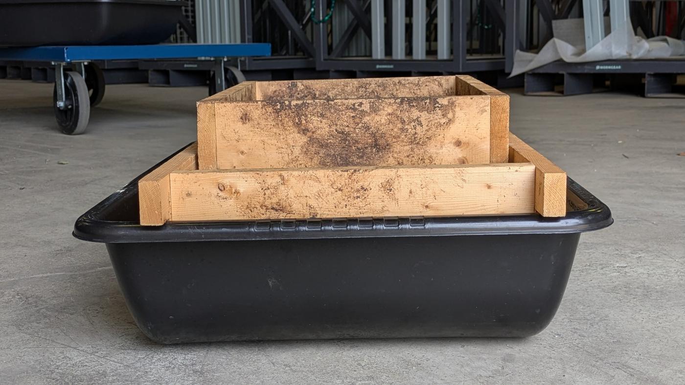 Side view of the wooden frame across the top of a black mixing tub, with the rolling screen sitting on the frame.